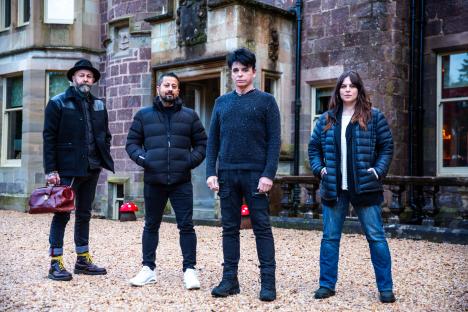 Gary Numan and three others standing outside a stone building.