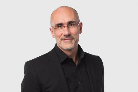 Portrait of a man in a black suit and glasses.