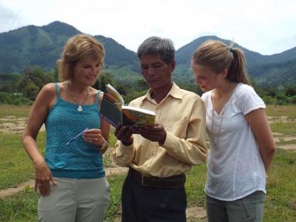 Three people looking at a book together outdoors.