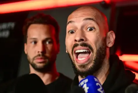 Close-up of a man with a surprised expression, another man is visible in the background.