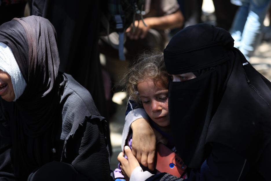 A woman embraces a child, another woman sits nearby with a bandage on her head.