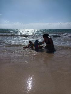 Woman playing with two children in ocean waves.