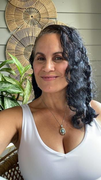 Woman with curly hair wearing a white tank top and necklace.