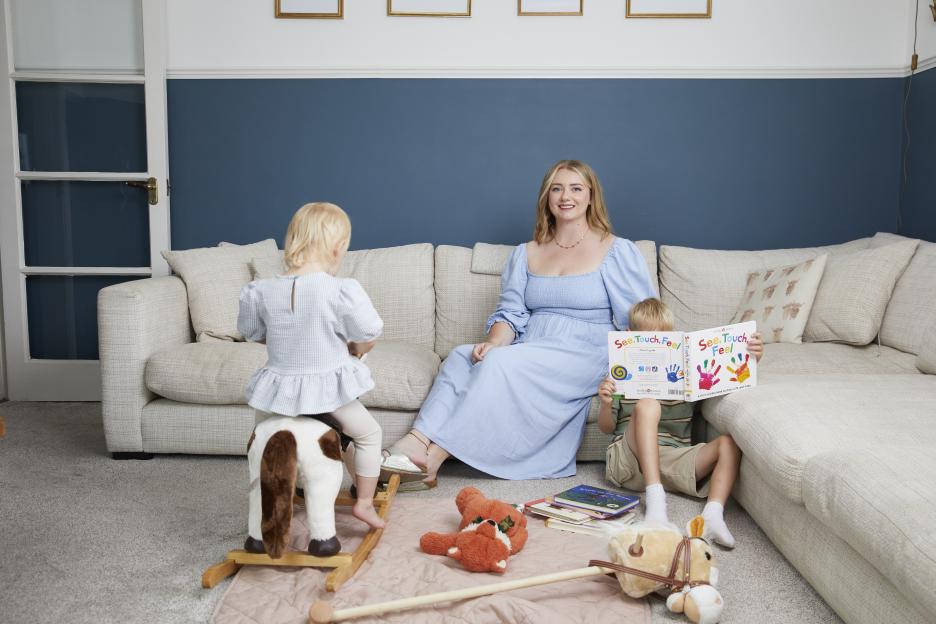 Woman with two young children on a couch reading a book.