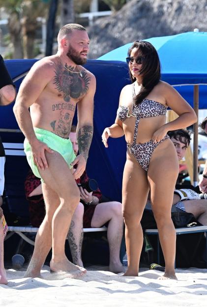 Conor McGregor on a beach with a woman in a leopard print swimsuit.