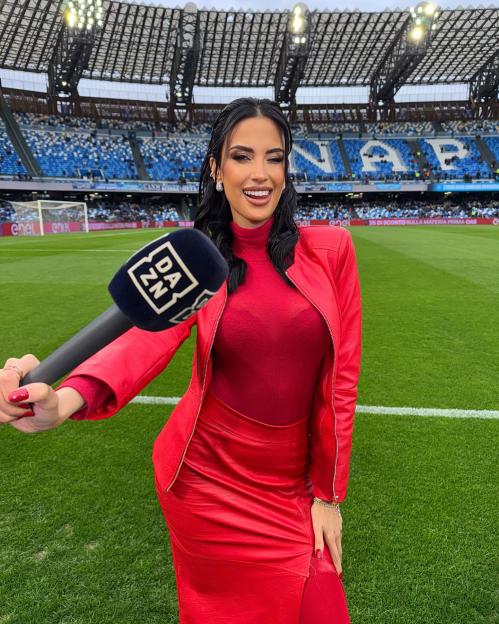 Woman in red holding a DAZN microphone at a soccer stadium.
