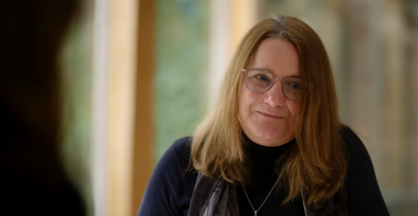 Woman with long brown hair wearing glasses, looking slightly to her right.