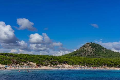 Cala Agulla beach in Mallorca, Spain, with people swimming and sunbathing.