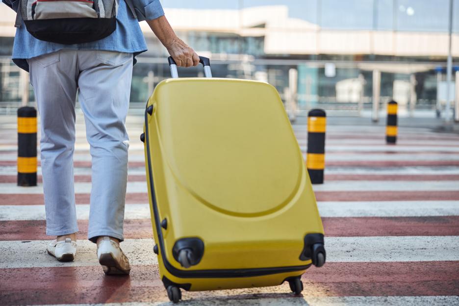 Woman pulling yellow suitcase across crosswalk.