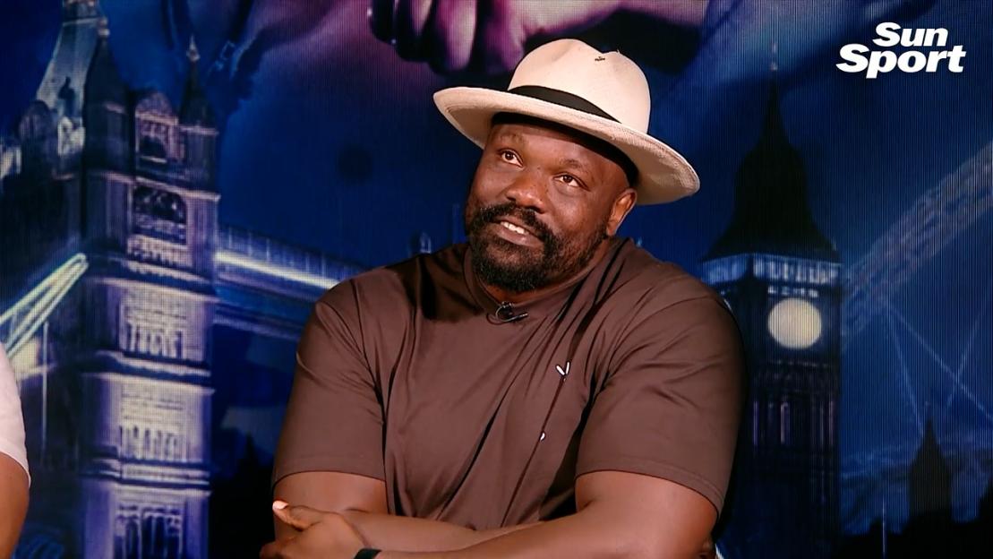 A man in a brown shirt and hat sits for an interview.