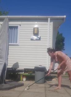 Woman sweeping patio outside caravan.