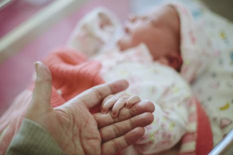 Newborn's hand grasping an adult's hand.