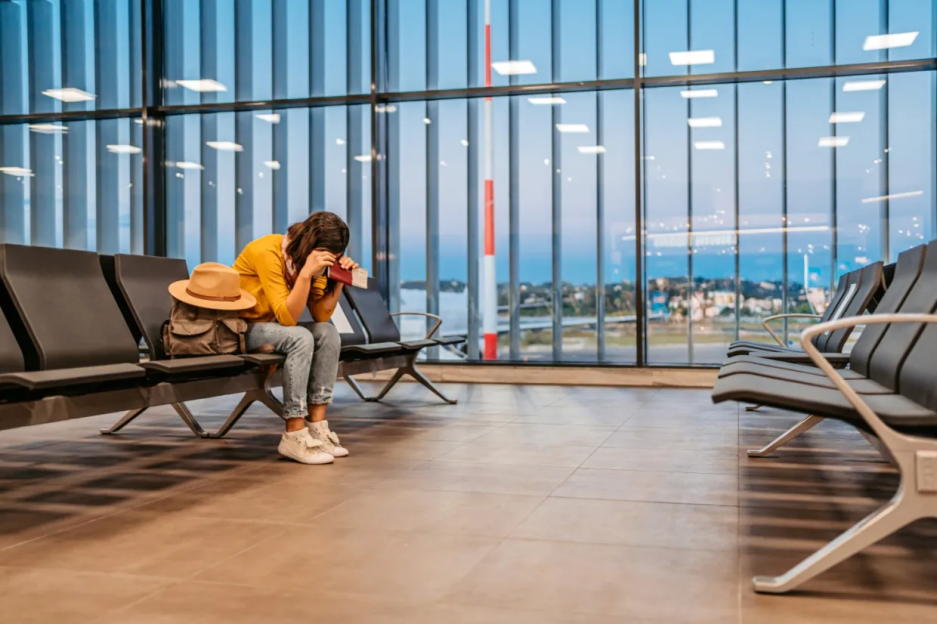 Woman sitting in airport terminal, head in hands.