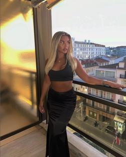 Woman in black crop top and skirt on balcony overlooking city.