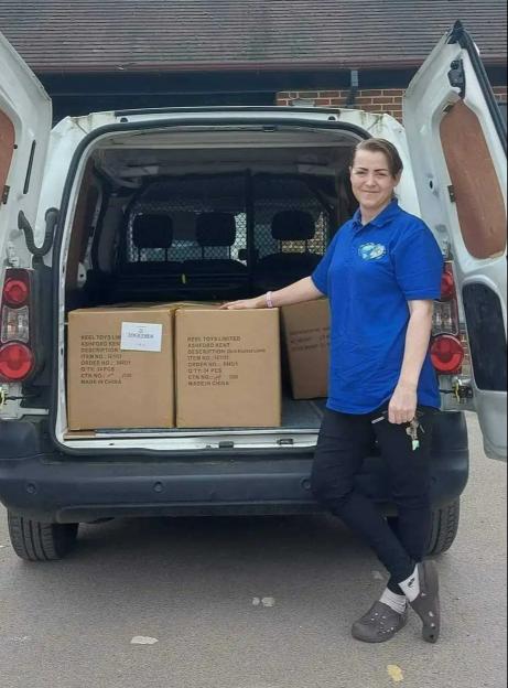 Woman standing by her van, which is loaded with boxes of toys.