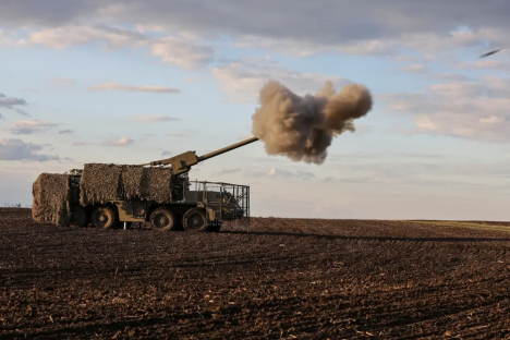 Camouflaged self-propelled howitzer firing in a field.