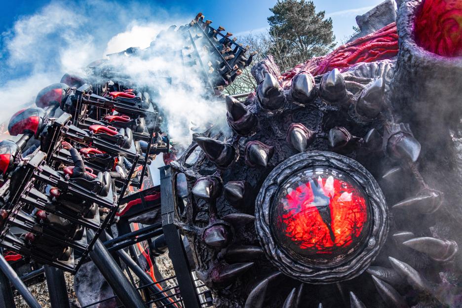 Rollercoaster cars passing a monstrous, smoke-filled creature with a glowing red eye.
