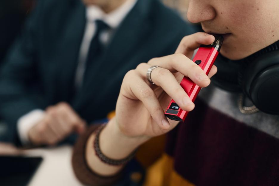 Close-up of a person vaping an electronic cigarette in an office.