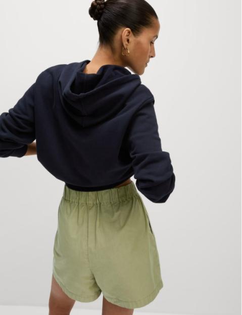Woman wearing olive green poplin shorts and a navy blue hoodie.