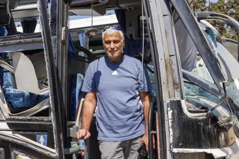 A man stands in the doorway of a damaged bus.