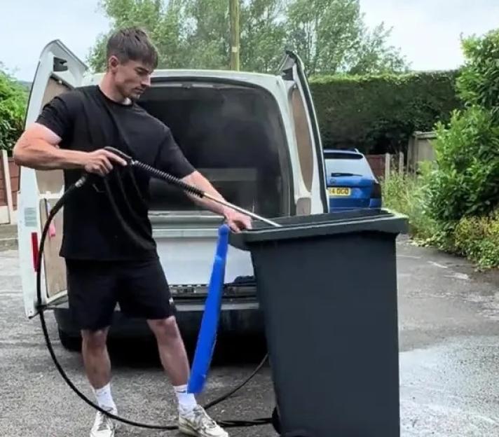 Man pressure washing a bin.