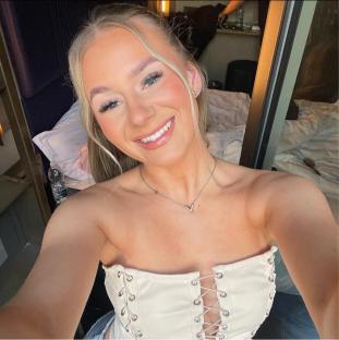 Selfie of a smiling young woman wearing a cream-colored corset top.