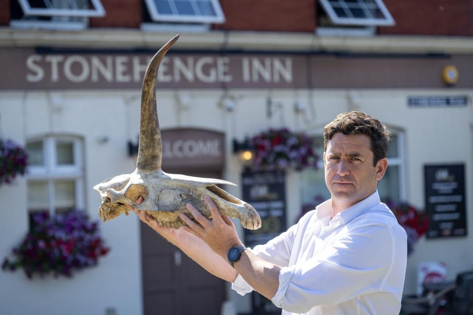 A man holding a skull with a long horn in front of the Stonehenge Inn.