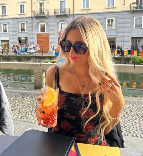 Woman with long blonde hair holding an Aperol Spritz at an outdoor cafe.
