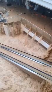 Floodwaters rushing through a shopping mall, submerging escalators.