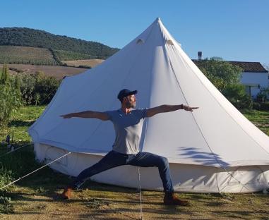 Man doing yoga in front of a tent.