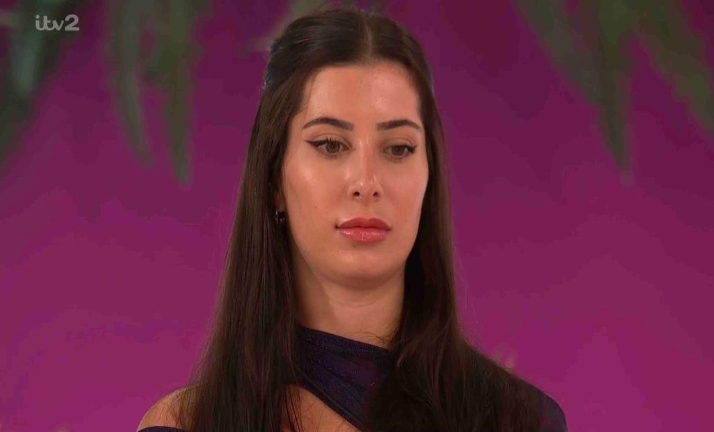 A woman with long dark hair looks at the camera.