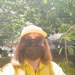 Woman wearing a yellow shirt, sunglasses, and a black face mask outdoors.