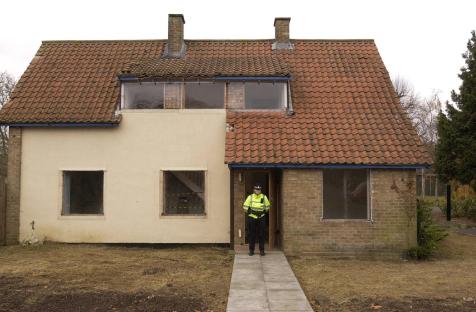A police officer stands outside a house under demolition.