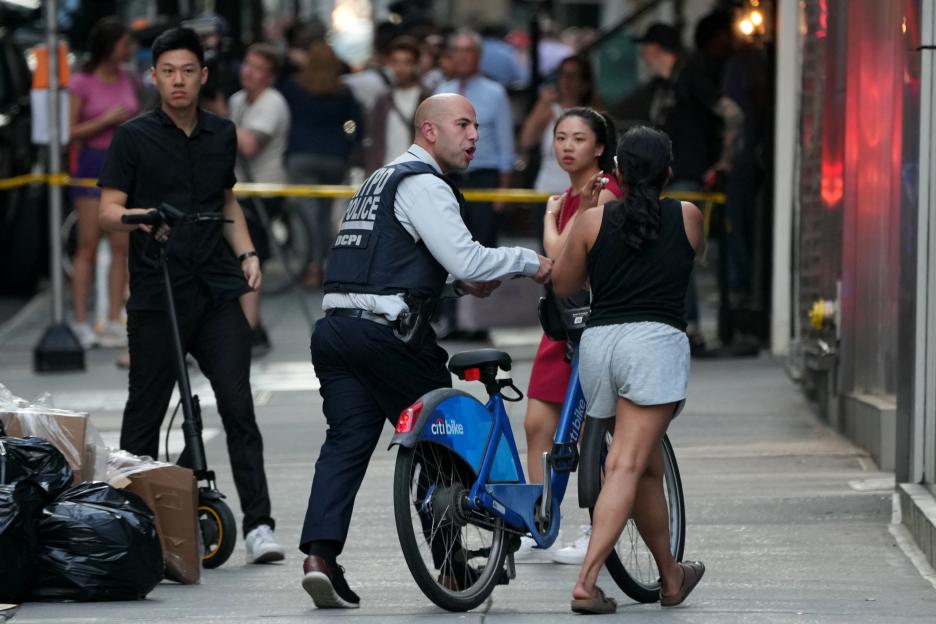 NYPD officer assisting a cyclist near a crime scene.