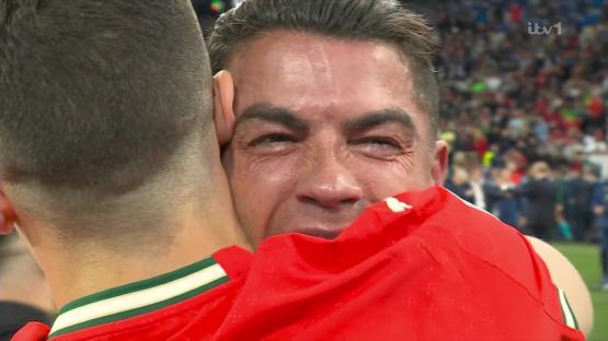 A man in a red jersey crying while embracing another man.