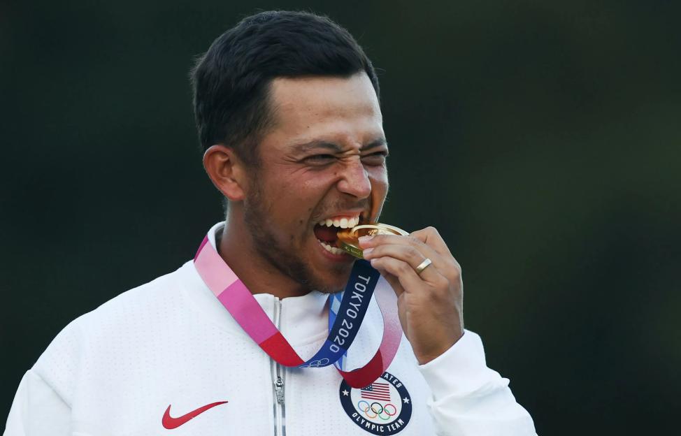 Xander Schauffele bites his gold medal at the Tokyo Olympics.