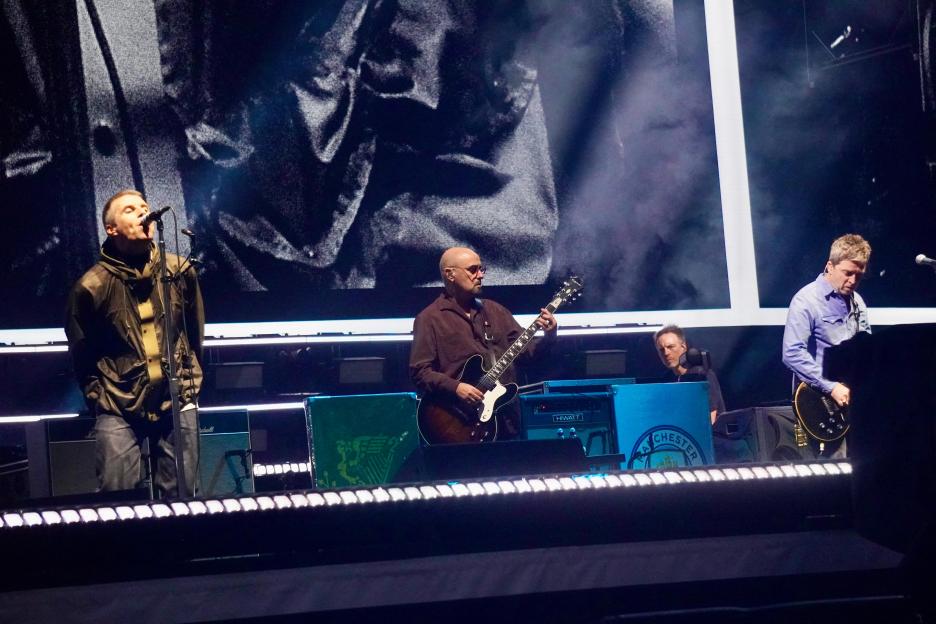 Noel Gallagher performing on stage with a red guitar.