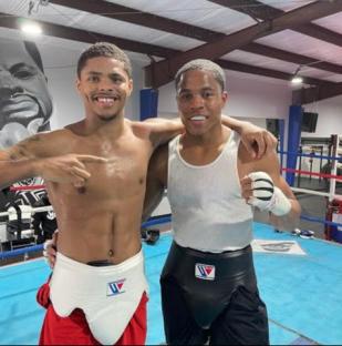 Two shirtless boxers in a boxing gym.