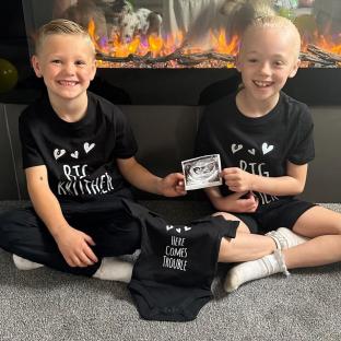 Two children holding an ultrasound image, announcing a new sibling.