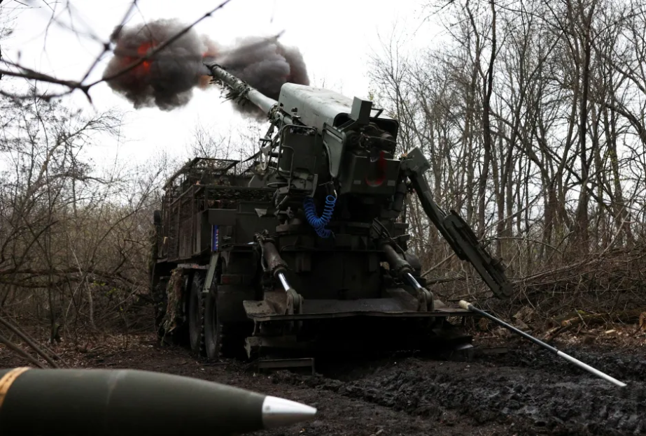 Self-propelled howitzer firing in a wooded area.