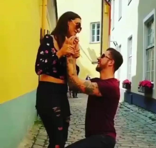 Woman accepting a marriage proposal from a man kneeling in a cobblestone alley.