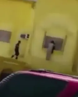 Two people running along a yellow building.