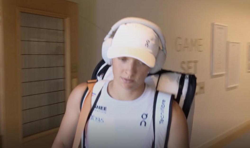Woman wearing headphones and a backpack walks down a hallway.