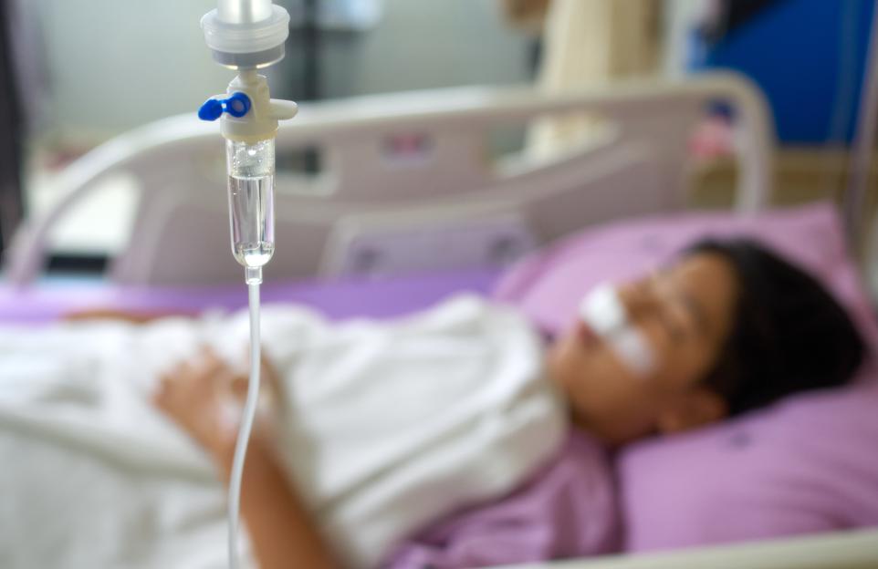 A saline drip above a blurred image of a teenage boy resting in a hospital bed.