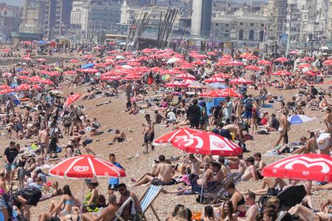 Crowded Brighton beach on a hot day, people under red umbrellas.