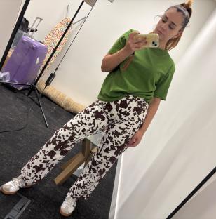 Woman in green shirt and cow-print pants taking a selfie.