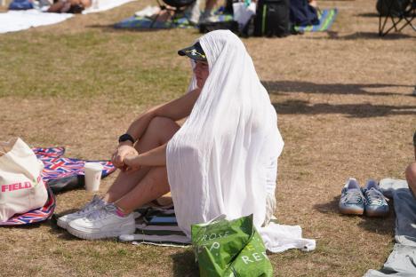 Tennis fan sitting on the grass in Wimbledon Park, covered by a white sheet to protect from the heat.