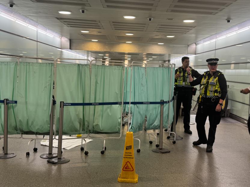 Police officers at St. Pancras station near medical privacy screens.