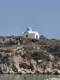 White and blue church on a rocky hillside overlooking a beach.