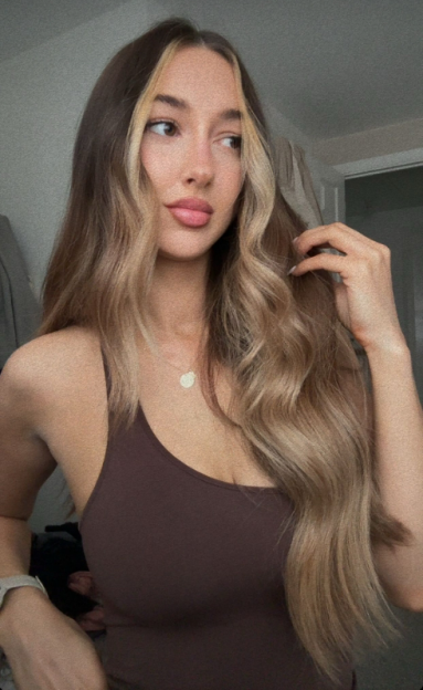 Woman with long brown hair and highlights wearing a brown tank top.